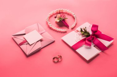 Alyans, inci kolye, yaka çiçeği ve pembe Pembe yüzeyi davetiye zarfları