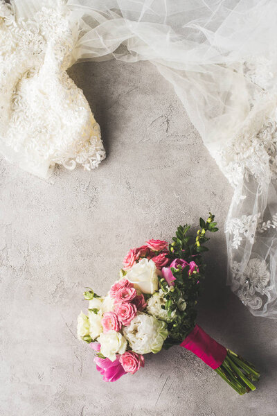 top view of wedding dress and bouquet on gray surface
