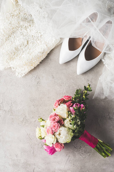 top view of wedding dress, shoes and bouquet on gray surface