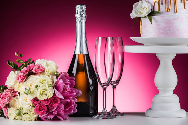 wedding bouquet, champagne and cake on stand on pink