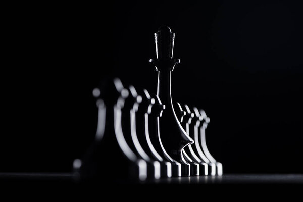 silhouettes of chess pawns and queen isolated on black, business concept