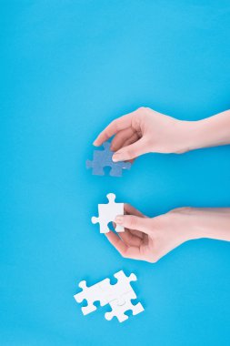 cropped image of businesswoman assembling blue and white puzzles isolated on blue, business concept clipart