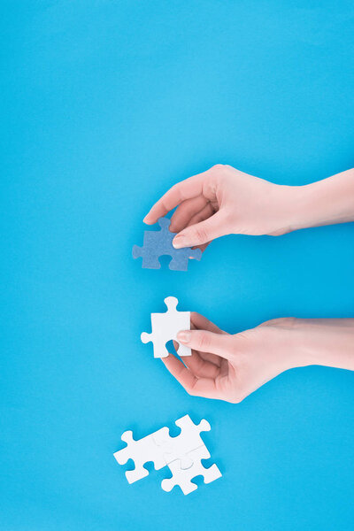 cropped image of businesswoman assembling blue and white puzzles isolated on blue, business concept