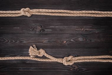 top view of arrangement of brown nautical ropes with knots on dark wooden tabletop clipart