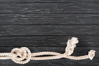 top view of white nautical rope with knots on dark wooden tabletop clipart