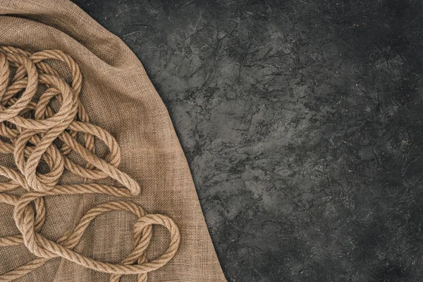 在深色混凝土表面上的麻布上排列的褐色航海绳索的顶部视图 — 图库照片