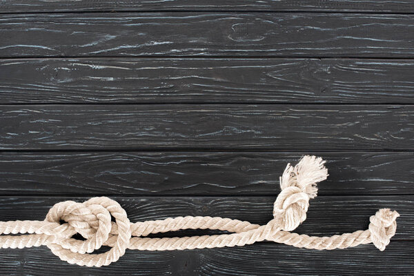 top view of white nautical rope with knots on dark wooden tabletop