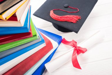 Mezuniyet şapka ve diploma yığılmış kitaplar tarafından beyaz masada