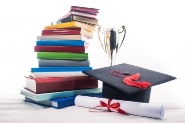 Graduation hat with diploma and trophy cup by stack of books clipart