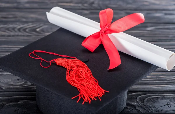 卒業の帽子と木製のテーブルに赤いリボンと卒業証書 — ストック写真