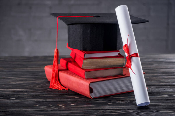 Graduation cap with diploma and books on table