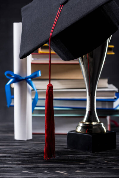 Graduation cap on trophy cup in front of books and diploma