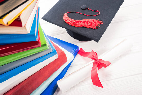 Graduation hat and diploma on white table by stacked books