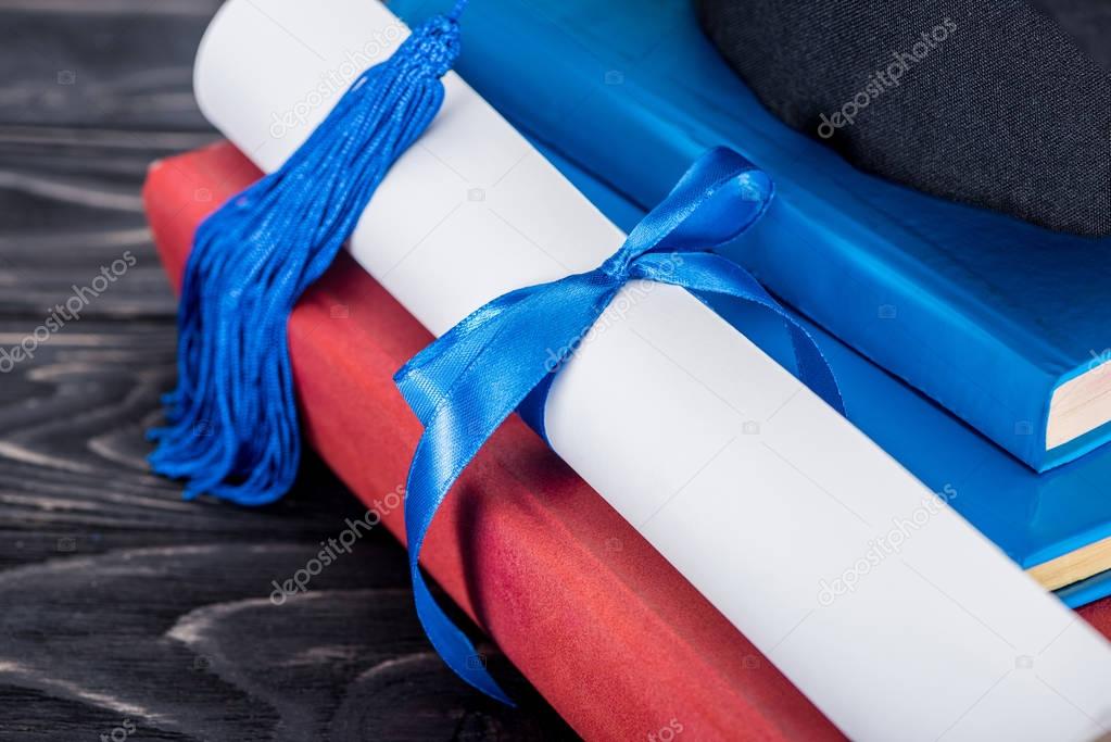 Graduation hat and diploma with blue ribbon on stack of books