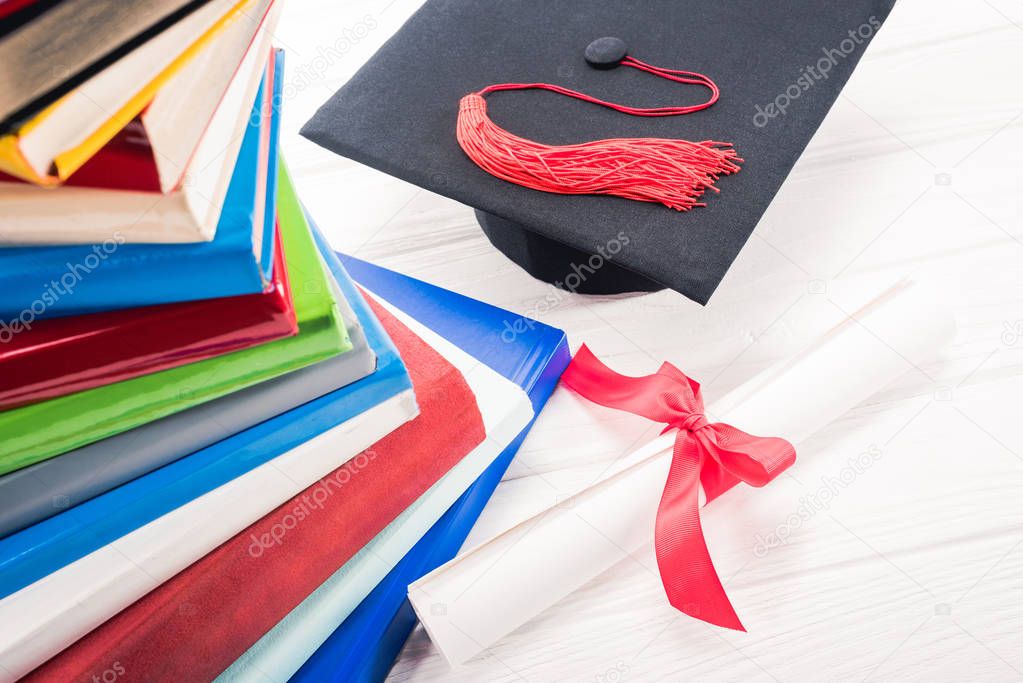 Graduation hat and diploma on white table by stacked books