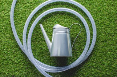 top view of watering can surrounded by hose on grass  clipart