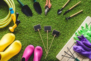 top view of empty blackboards surrounded by rubber boots, gardening equipment and protective gloves on grass clipart
