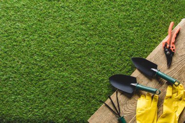 top view of shovels, hand rake, protective gloves and secateurs on wooden planks clipart