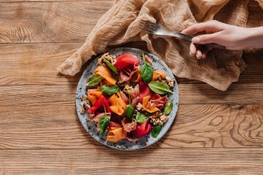 çatal ve midye, sebze ve jamon salatası ahşap masa üzerinde tutan insan el atış kırpılmış