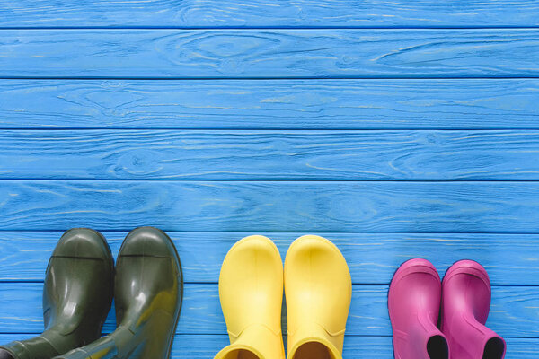 top view of colorful rubber boots placed in row on blue wooden planks