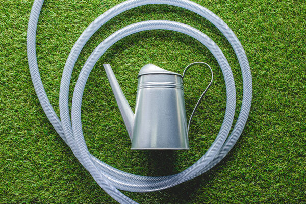 top view of watering can surrounded by hose on grass 