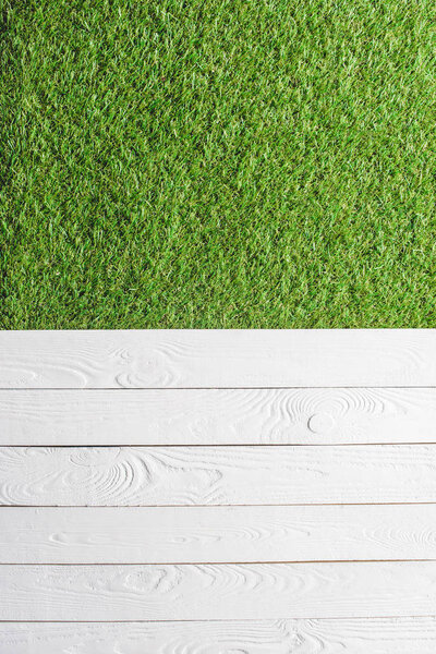 top view of green lawn and white wooden planks background 