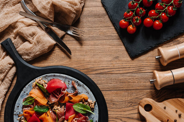 Salad with mussels, vegetables and jamon, fork with knife and fresh tomatoes on wooden table