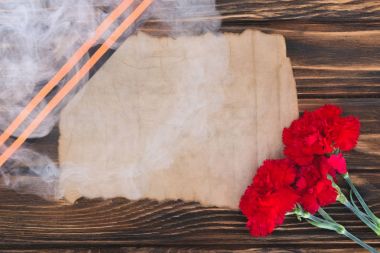 smoke over st. george ribbon, old empty paper and carnations on wooden surface clipart
