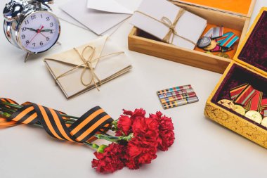 closeup shot of carnations wrapped by st. george ribbon, letters, medals in boxes and alarm clock, victory day concept  clipart