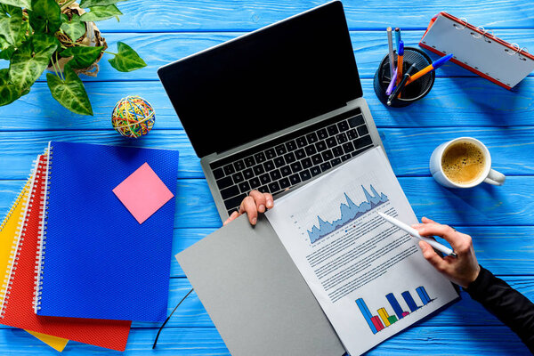 Крупный план человека, изучающего карты на ноутбуке на синем деревянном столе с канцелярскими принадлежностями
