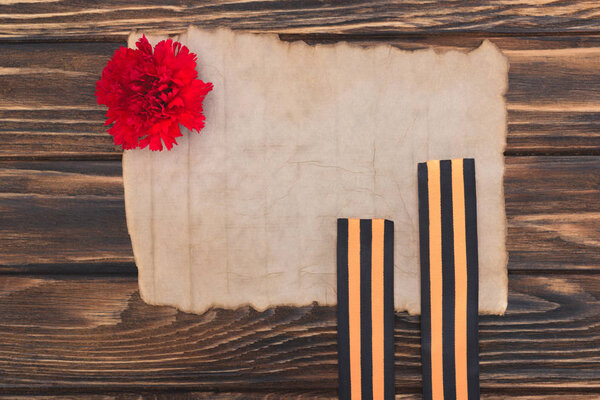 top view of old empty paper, carnation and st. george ribbons on wooden surface
