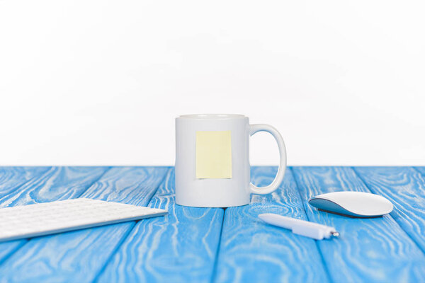 closeup shot of empty note paper on cup, pen, keyboard and mouse on wooden surface