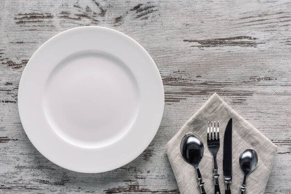 White plate and cutlery on napkin on wooden background