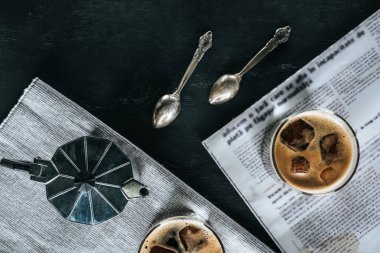 düz lay ile kahve makinesi, kaşık, gazete ve soğuk demlenmiş kahve siyah masa üzerinde bardak