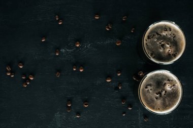 top view of glasses of cold brewed coffee with ice on dark surface with roasted coffee beans around clipart