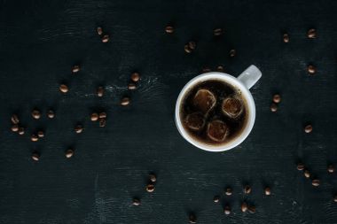 top view of mug of cold iced coffee on dark tabletop with roasted coffee beans around clipart