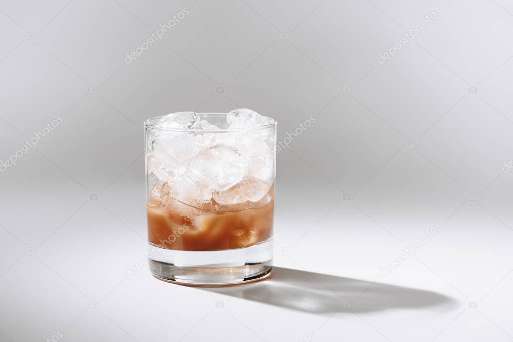 close up view of glass of cold brewed coffee with ice cubes on white tabletop