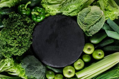 top view of black cutting board between green vegetables, healthy eating concept clipart