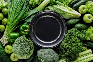 top view of black plate between green vegetables, healthy eating concept clipart