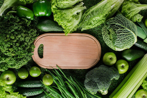 top view of cutting board between green vegetables and fruits, healthy eating concept