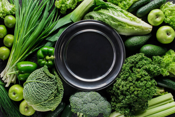 top view of black plate between green vegetables, healthy eating concept