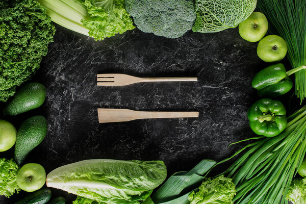 top view of wooden spatula and fork between green vegetables, healthy eating concept