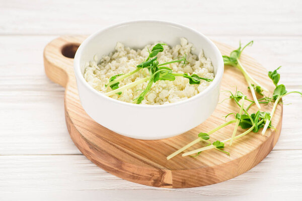 close-up view of bowl with fresh healthy cottage cheese with sprouts on wooden board 