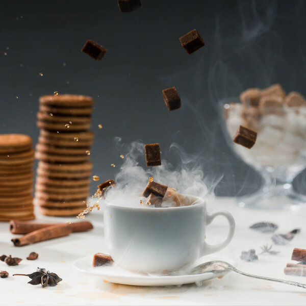 Close-up of brown sugar cubes falling into coffee cup with splashes