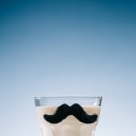 Transparent glass with mustaches filled with milk isolated on blue background