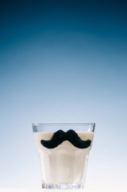 Transparent glass with mustaches filled with milk isolated on blue background clipart