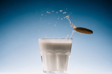 Cracker cookies splashing into glass of milk on blue background clipart