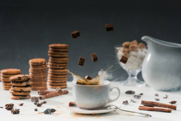 Coffee cup with splashing cane sugar on table with cookies and spices