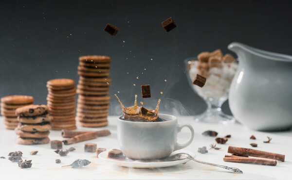 Brown sugar cubes falling in cup with black coffee on table with cookies and spices