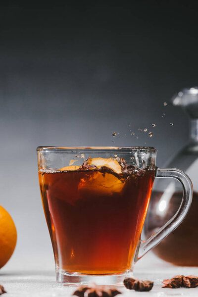 Hot black tea in cup with lemon pieces and splashes